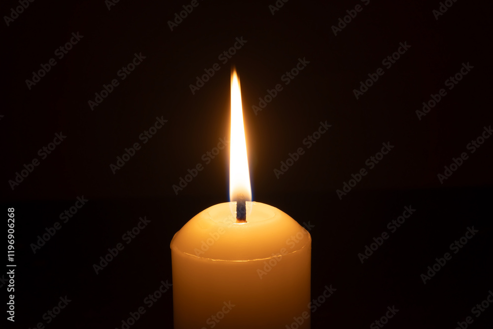 A single burning candle flame or light glowing on a big white candle isolated on black or dark background on table in church for Christmas, funeral or memorial service A single burning candle flame or light glowing on a big white candle isolated on black or dark background on table in church for Christmas, funeral or memorial service
