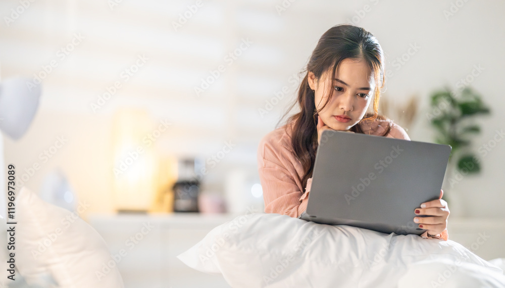 Woman working on a laptop in a cozy bedroom during evening hours while enjoying a relaxed atmosphere Woman working on a laptop in a cozy bedroom during evening hours while enjoying a relaxed atmosphere