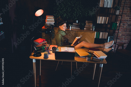 Young woman in casual sneakers and a stylish jumper relaxes at home, reading a book in a cozy photo