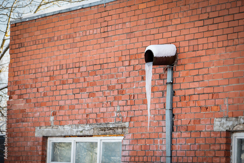 Large icicles hanging from a metal gutter, indicating heat loss and poor energy efficiency. Red brick wall photo