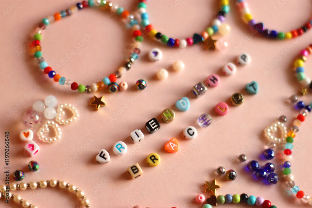 Friendship bracelet spelled with letter beads. Colorful handmade bracelets and various beads. Selective focus, pink background.