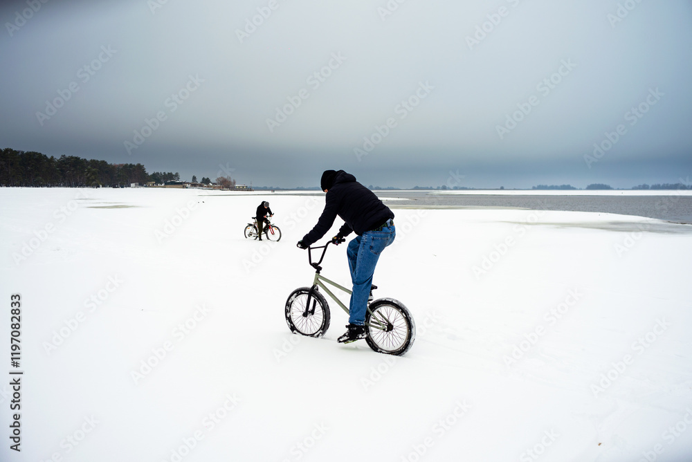 Fototapeta premium Two teenagers ride bicycles in the snow in winter.