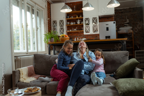 Two daughters are tickling their mother on the sofa in their living room, enjoying a playful and joyful moment together, creating a heartwarming scene of family bonding photo