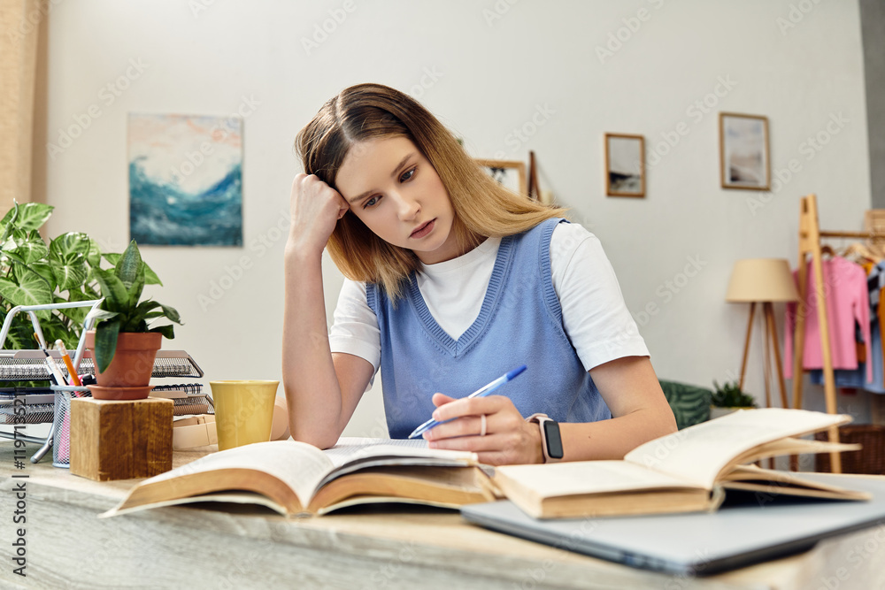 A focused teenage girl studies diligently at her desk, surrounded by home comforts. A focused teenage girl studies diligently at her desk, surrounded by home comforts.