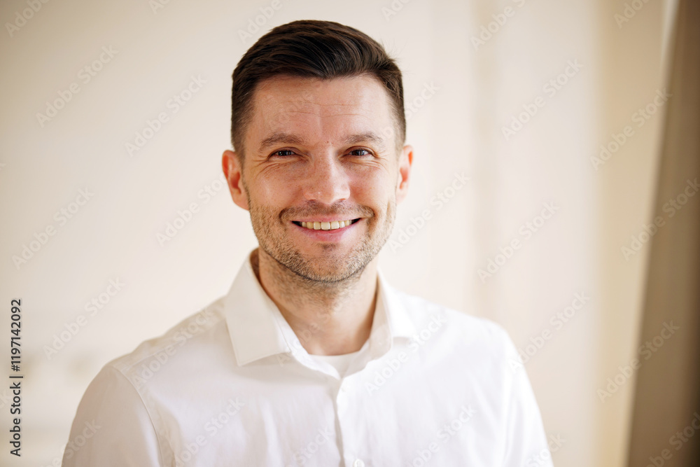 Smiling man in a white shirt poses for a casual portrait in a bright indoor setting Smiling man in a white shirt poses for a casual portrait in a bright indoor setting