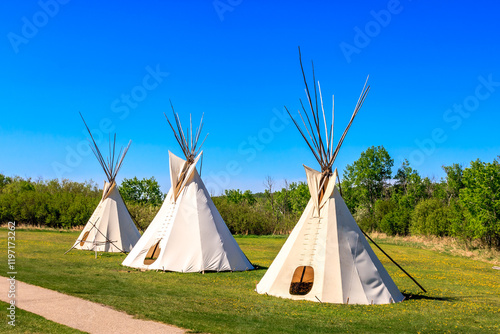 Three teepees are standing in a field with a blue sky above them photo