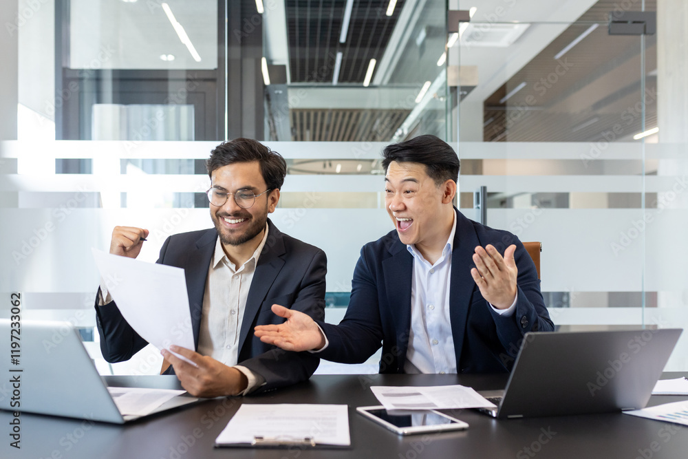Two business colleagues behind paperwork rejoicing and celebrating victory triumph and successful achievement results. Men in business suits sitting at desk reviewing financial investment reports. Two business colleagues behind paperwork rejoicing and celebrating victory triumph and successful achievement results. Men in business suits sitting at desk reviewing financial investment reports.