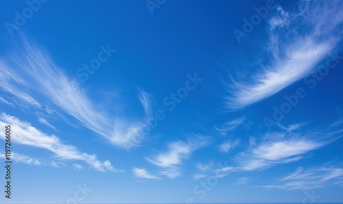Wispy white clouds drift across a vibrant blue sky over a calm sea