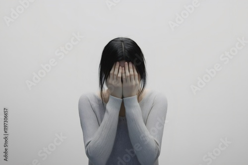 Scared woman hiding her face with hands, conveying deep fear and shame against a stark white background, reflecting emotional turmoil