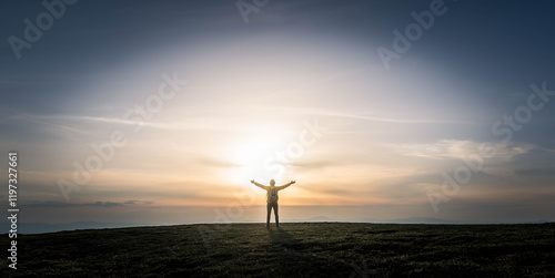 Happy man with arms up standing on top of the mountain at sunset