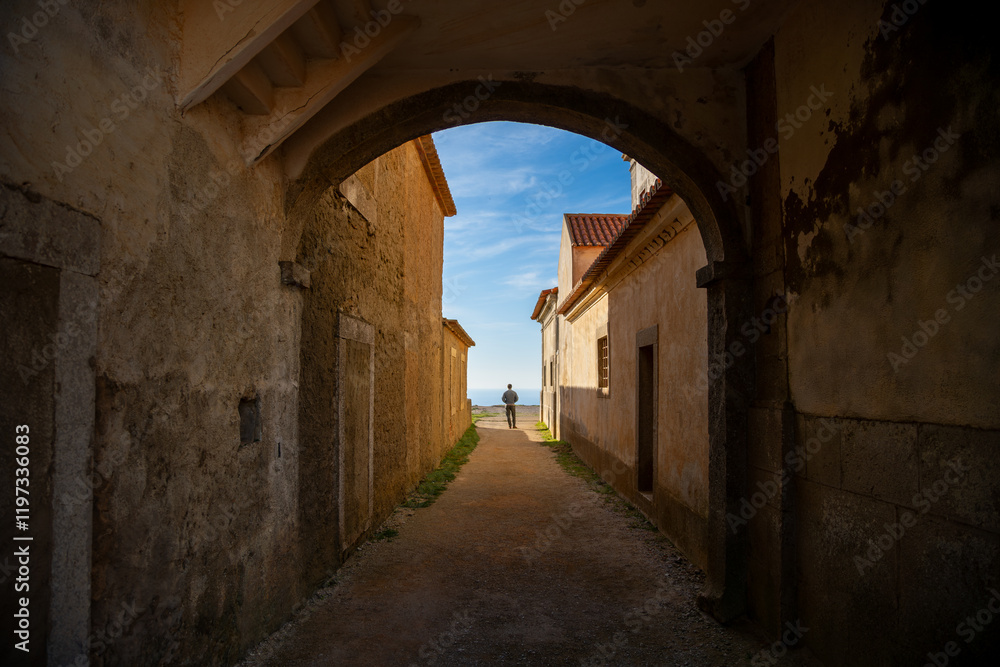 Naklejka premium Silhouette of a Man Standing in an Archway Overlooking the Ocean at Santuário de Nossa Senhora do Cabo Espichel, Portugal. December 2024