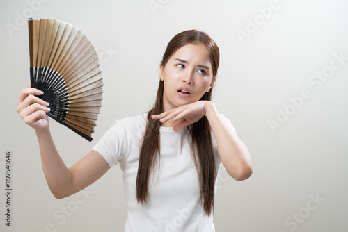 Suffering summer heat wave stroke, hot weather, tired asian young woman sweaty and thirsty, refreshing with hand in blowing, wave fan to ventilation when temperature high, isolated on background. photo