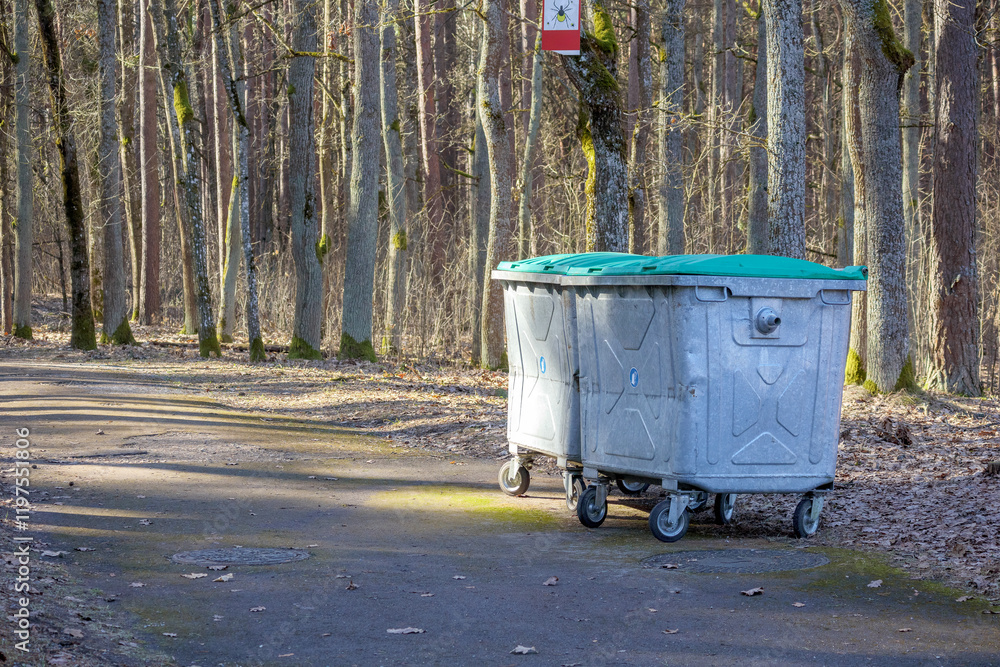 a large gray waste container with a green lid placed on a forest path next to trees.
a large gray waste container with a green lid placed on a forest path next to trees.