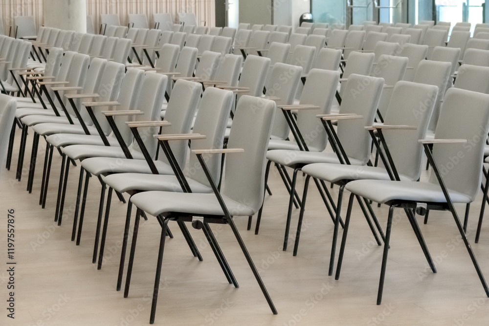 Fototapeta premium An empty fragment of a conference hall or auditorium with rows of gray chairs with wooden arms.