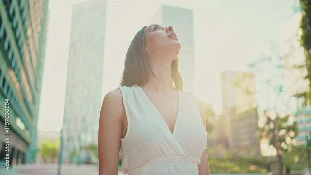 Lovely young woman with freckles and dark loose hair wearing white top and jeans is enjoying the view of modern city. Beautiful girl with long eyelashes looks at the upper floors of building Lovely young woman with freckles and dark loose hair wearing white top and jeans is enjoying the view of modern city. Beautiful girl with long eyelashes looks at the upper floors of building