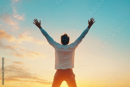 Man celebrates sunset with raised arms against a vibrant sky in an open landscape