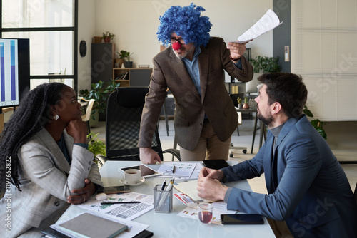 Obraz na plátně Mature confident director of business company in clown wig looking at young fema