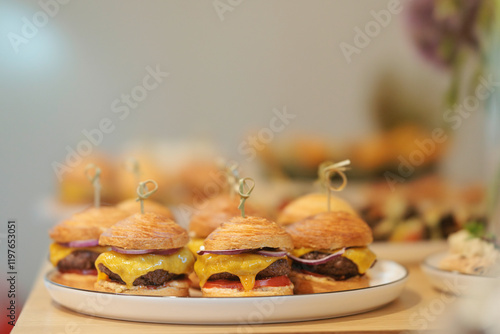 A delightful assortment of cheeseburgers, each nestled in a buttery croissant, are elegantly displayed on a white platter, inviting appetites at a lively gathering