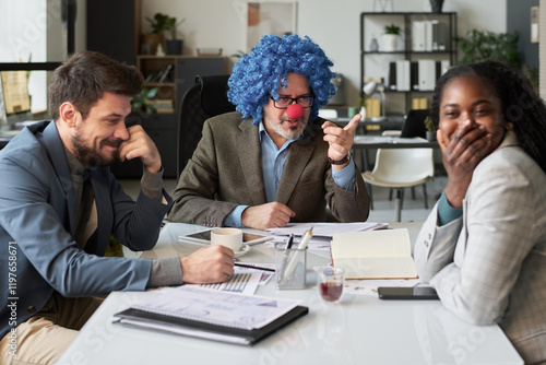 Young African American female employee covering mouth with hand while laughing at strict clown boss pointing at her photo