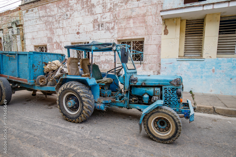 An old blue tractor with a trailer parked on a street in Cuba. An old blue tractor with a trailer parked on a street in Cuba.