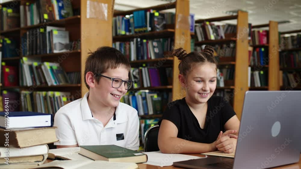 Two children studying together with a laptop in the library, participating in an online lesson. Perfect for themes of online learning, teamwork, and education. Two children studying together with a laptop in the library, participating in an online lesson. Perfect for themes of online learning, teamwork, and education.