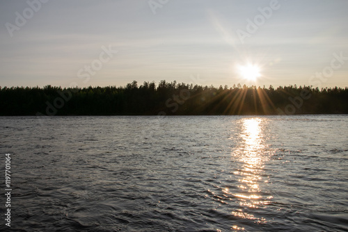 Sunset over forest and river with sunlight reflections on water. Etuväylä river glistening under sunset in Finland, Scandinavia. 