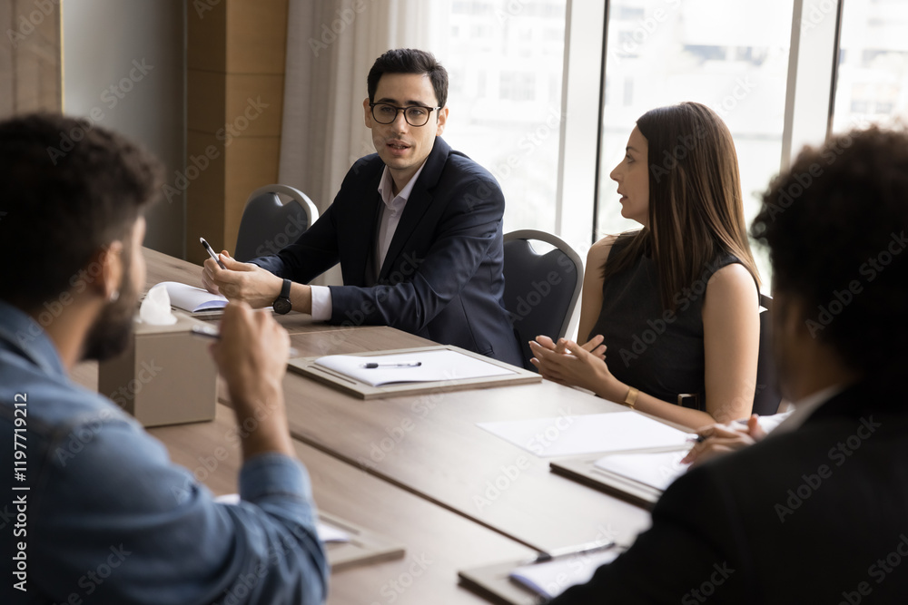 © fizkes - Group of serious professional businesspeople solve business-related issue or challenges gathered in boardroom. Arabian businessman conduct team meeting with stakeholders, provide information and ideas