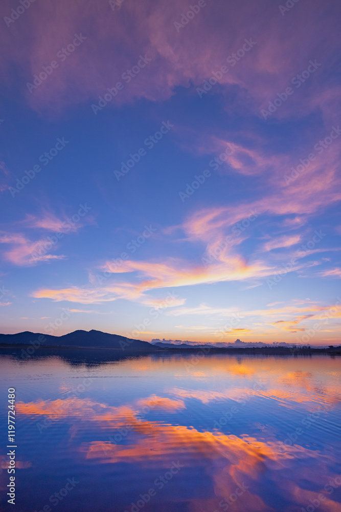Fototapeta premium Landscape of mountains and lake at sunset and clouds reflected in the water.