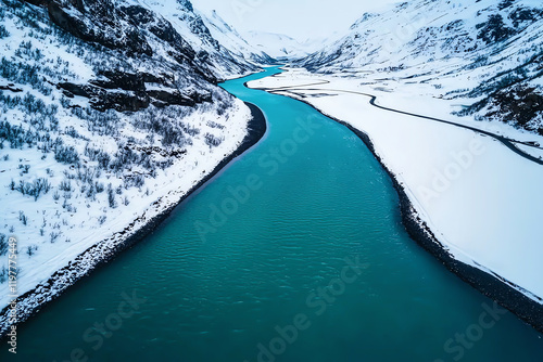 A stunning aerial view of a river cutting through a snow-covered valley, showcasing the contrast between the turquoise water and the white landscape. photo