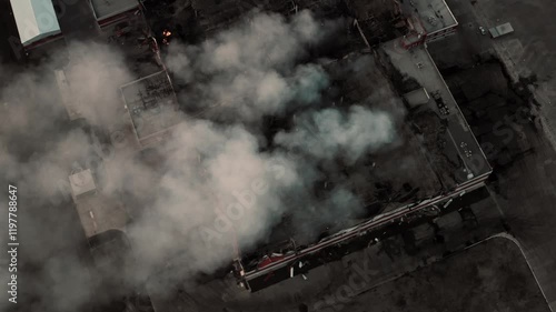 Aerial top view of city block on fire with thick smoke rising, damaged rooftops and urgent rescue situation from drone vantage, urban disaster.