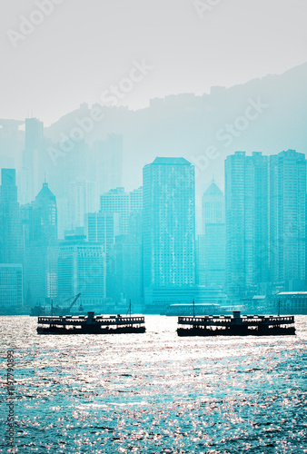 South across Hong Kong Harbour. Two Star Ferry passenger boats silhouetted in front of Hong Kong Island city centre buildings photo