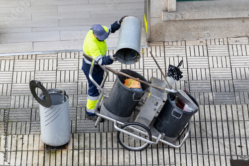Cleaning worker emptying the trash into his cleaning cart on a city sidewalk