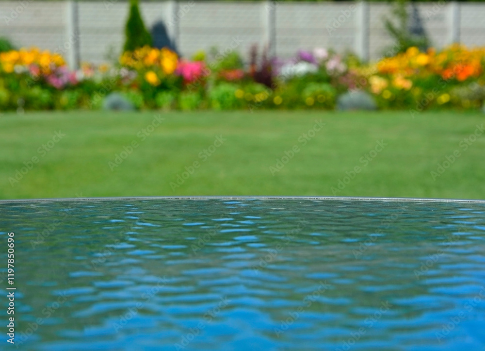 niebo odbite w szklanym blacie stołu na tle ogrodu z trawnikiem i kwiatami, sky reflected in the glass table against the background of garden with flowers, blue sky reflected in glass table, iluzja