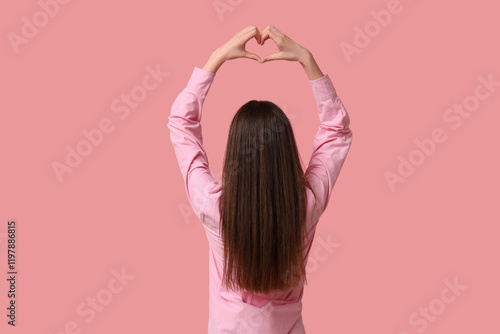 Young woman making heart gesture on pink background, back view