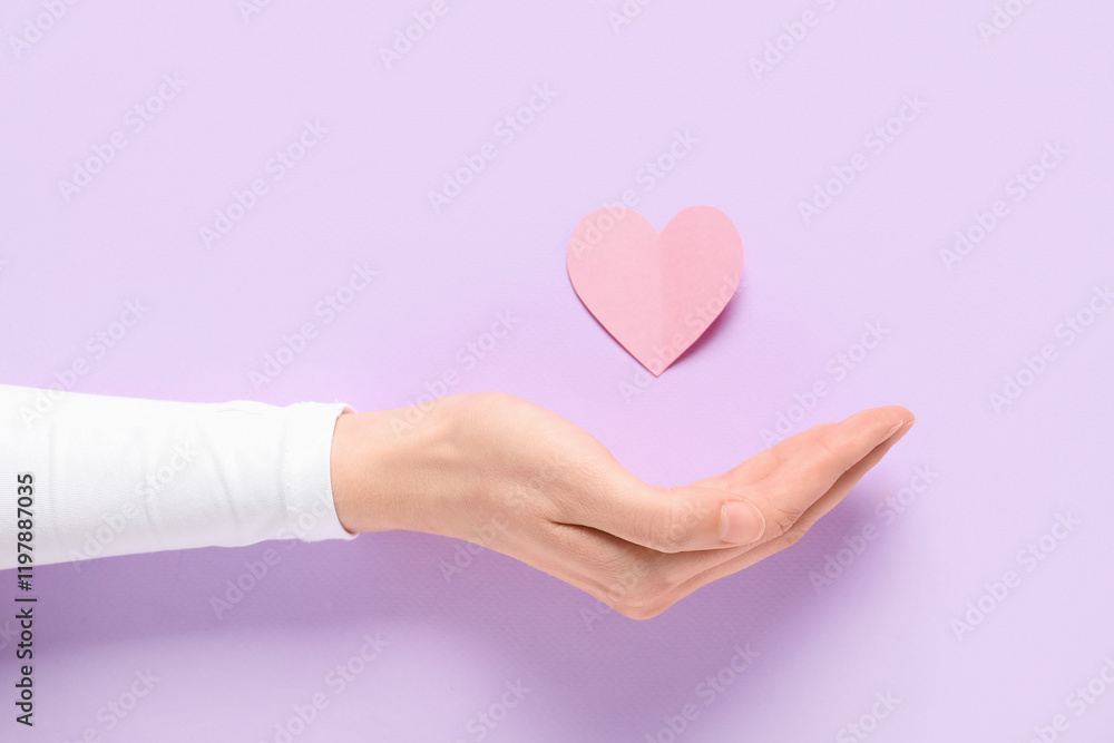 Female hand with paper heart on lilac background, closeup. Valentine's Day celebration Female hand with paper heart on lilac background, closeup. Valentine's Day celebration