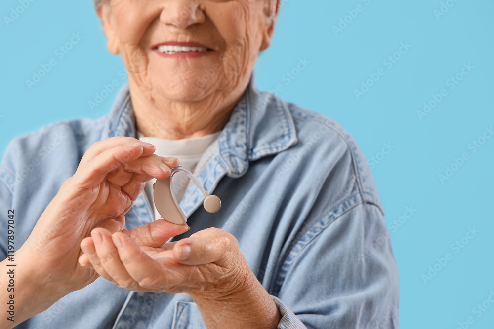Fototapeta premium Senior woman with hearing aid on blue background, closeup