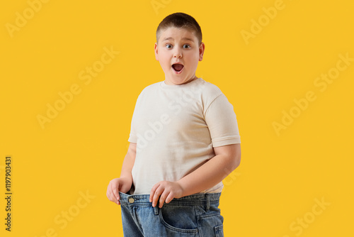 Surprised overweight boy in loose jeans on yellow background. Diet concept