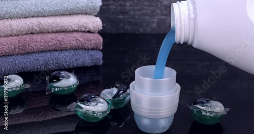 Liquid detergent flowing from the bottle into the container in front of the towels. Laundry and freshness concept. Slow motion 4k