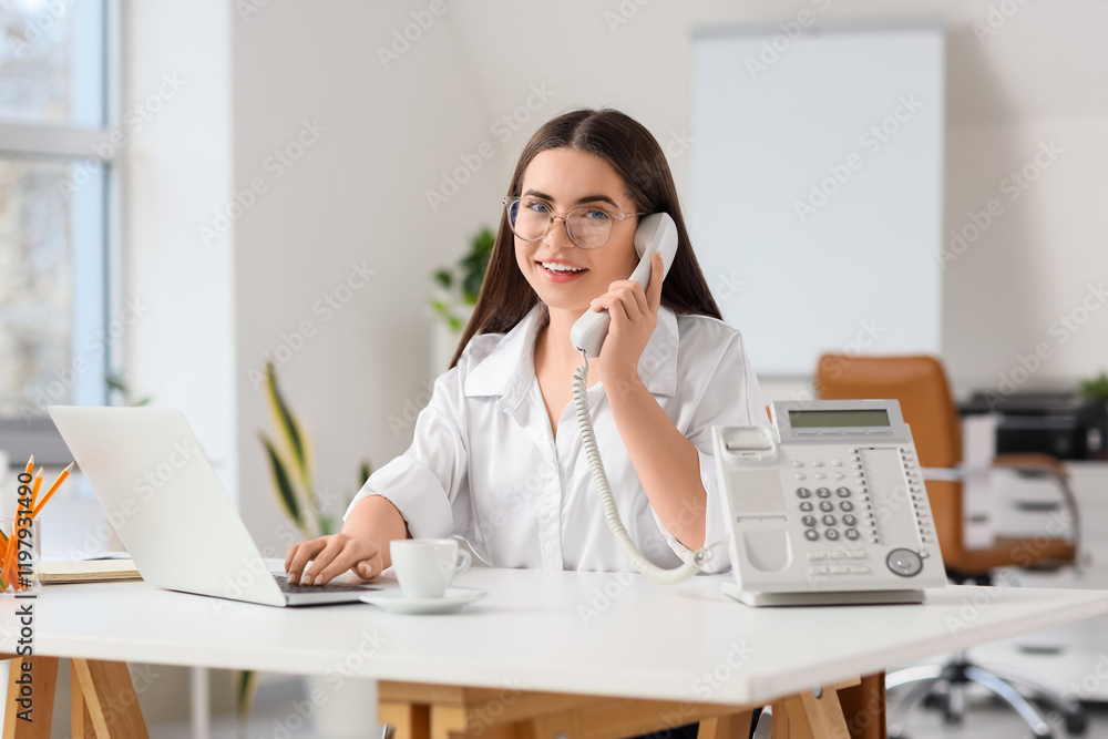Young secretary with laptop talking by telephone at table in office Young secretary with laptop talking by telephone at table in office