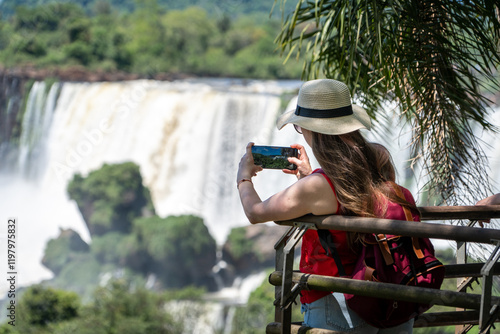 Mujer turista de espaldas, tomando una foto a las cataratas del Iguazú, en el Parque Nacional Iguazú, Argentina	 photo