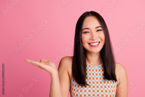 Cheerful young woman presenting with open palm against a pink background photo