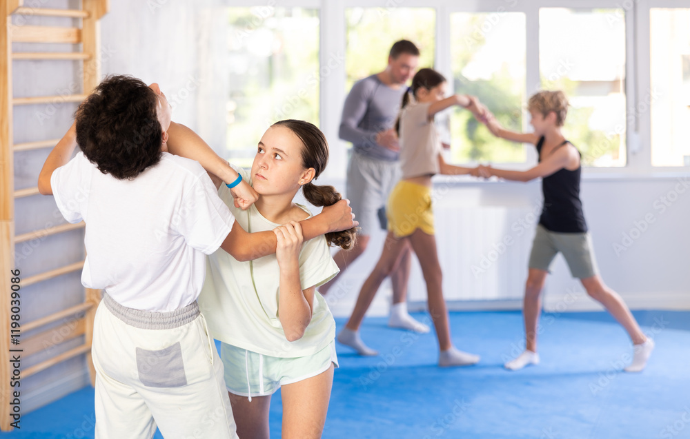 Boy and girl practicing self-defense techniques in group at gym Boy and girl practicing self-defense techniques in group at gym