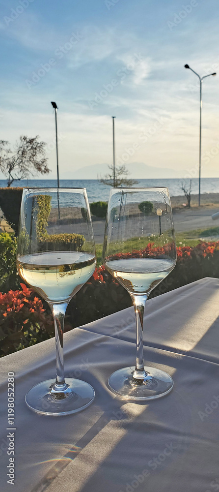 Obraz premium two glasses of white wine on a table in a cafe by the sea. aperitif before dinner. resort cafe on the seashore. beauty in nature and dinner at sunset