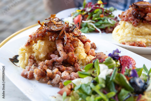 Traditional Danish dish - Burning love (Brændende kærlighed) consisting of mashed potatoes topped with fried bacon and onions, with a berry and flower salad on a white plate