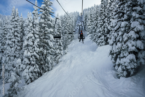 Snowboarder riding a chairlift through the snow covered mountains of Steamboat Springs Colorado photo