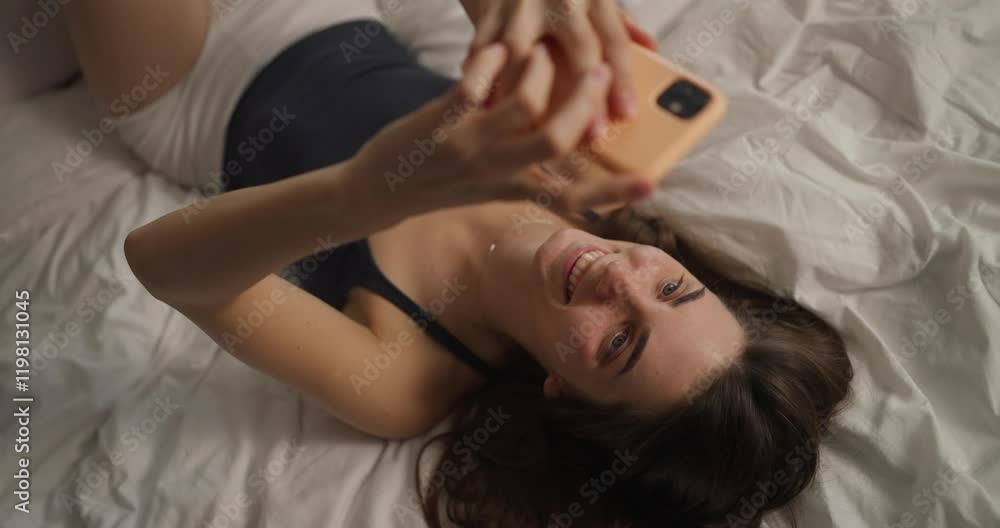 Close-up of a happy girl with a yellow smartphone communicates on social networks after waking up in a white bed in the morning Close-up of a happy girl with a yellow smartphone communicates on social networks after waking up in a white bed in the morning