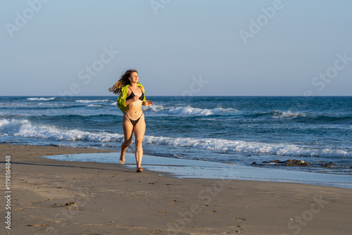 Young white woman in black bikini on the beach at sunset