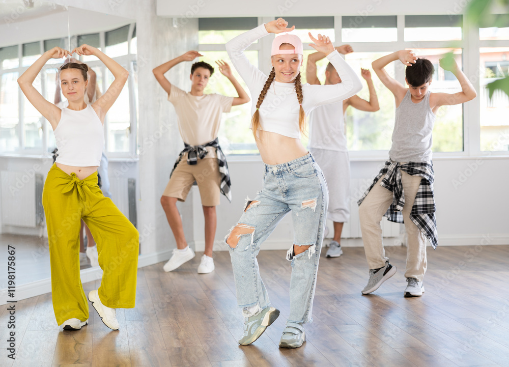Naklejka premium Happy teenage girl practicing basic hip-hop moves in training hall during group dancing classes