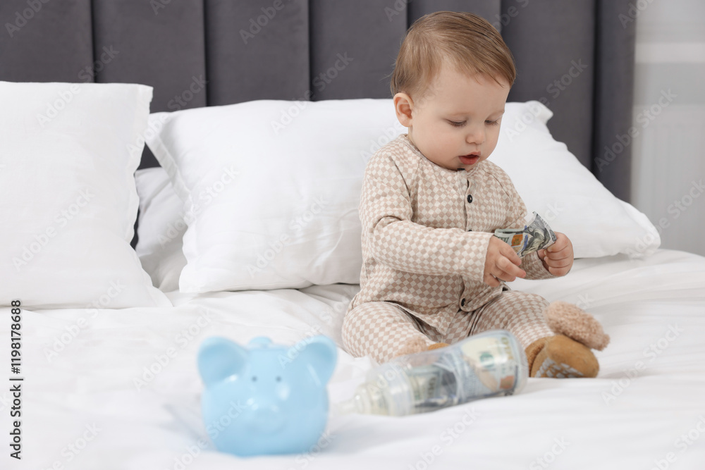 Cute little baby with money in bottle and piggybank on bed at home. Space for text Cute little baby with money in bottle and piggybank on bed at home. Space for text