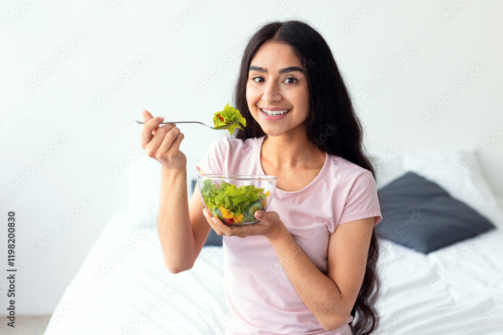 Healthy nutrition concept. Beautiful Indian woman eating yummy vegetable salad while sitting on bed at home. Portrait of young Hindu lady having vegetarian meal, taking care of her body Healthy nutrition concept. Beautiful Indian woman eating yummy vegetable salad while sitting on bed at home. Portrait of young Hindu lady having vegetarian meal, taking care of her body